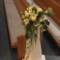 White floral arrangement with greenery on a wooden church pew