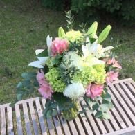 Bouquet of pink, white, and green flowers arranged on a wooden table outdoors