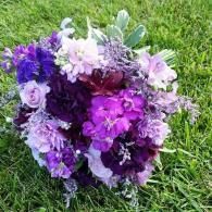Purple and white bouquet of flowers resting on green grass