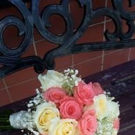 Bouquet of pink, yellow, and white roses on a dark bench against a tiled wall.