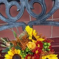 Colorful bouquet of yellow, red, and orange flowers against a decorative metal railing and brick wall