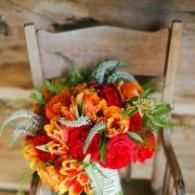 Bright orange and red flower bouquet arranged on a wooden chair indoors