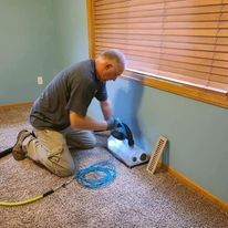 A man is kneeling on the floor in a room using a vacuum cleaner.