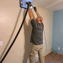 A man is using a vacuum cleaner to clean a wall.