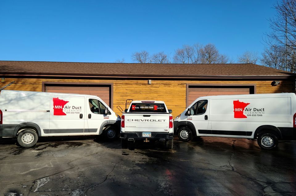 Three white vans and a truck are parked in front of a building.