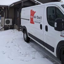 A white van is parked in the snow in front of a building.