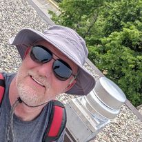 A man wearing a hat and sunglasses is standing on a roof.