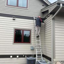 A man is standing on a ladder on the side of a house.