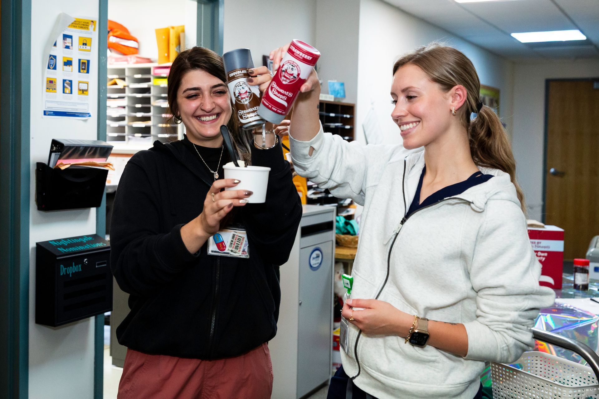 Two women smiling, one squirts whipped cream onto a cup held by the other.