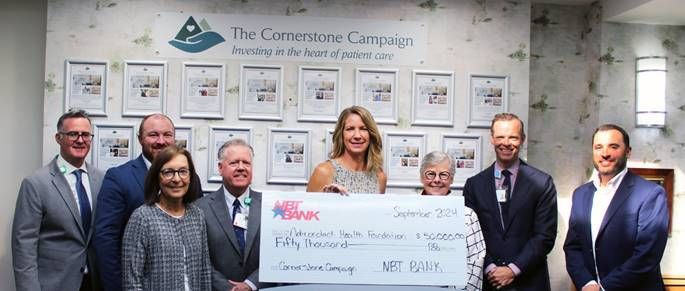 Group of people holding a large check in a light-colored room. The check says 