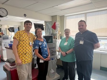 Four healthcare workers in scrubs pose by medical equipment in a hospital room.