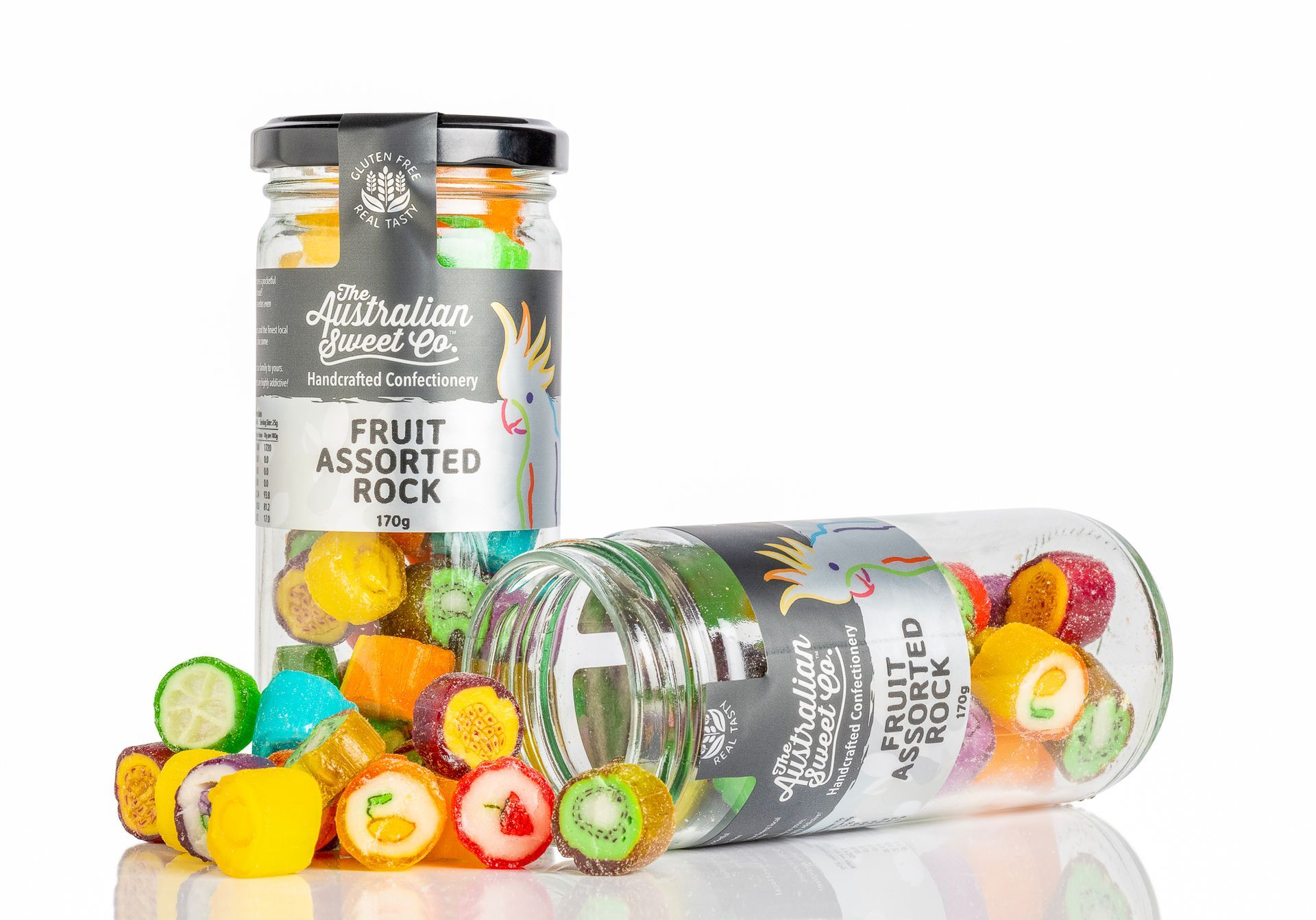 Two jars of colorful fruit assorted hard candies, one upright and one lying on its side, spilling candies out