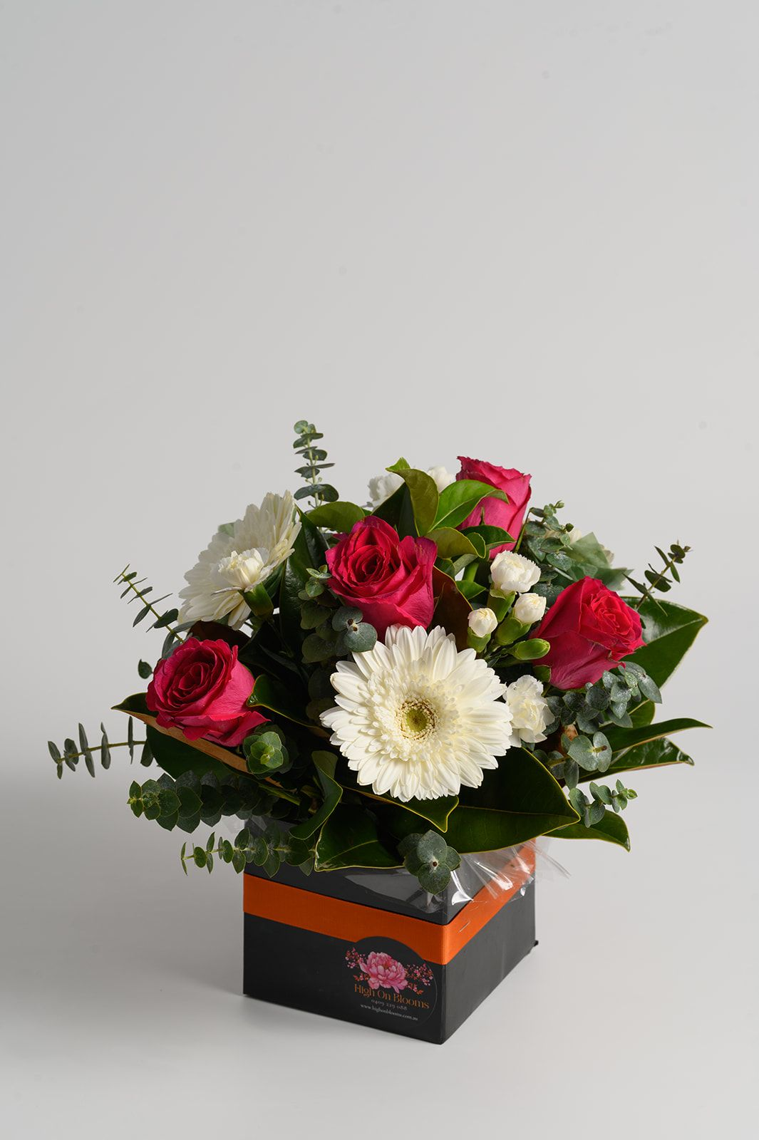 Mixed bouquet of pink, red, and white flowers in a black and orange gift box