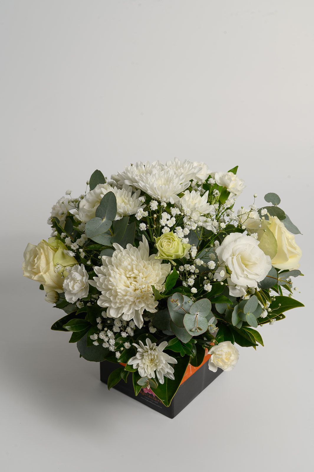 White floral bouquet with greenery in a black square vase