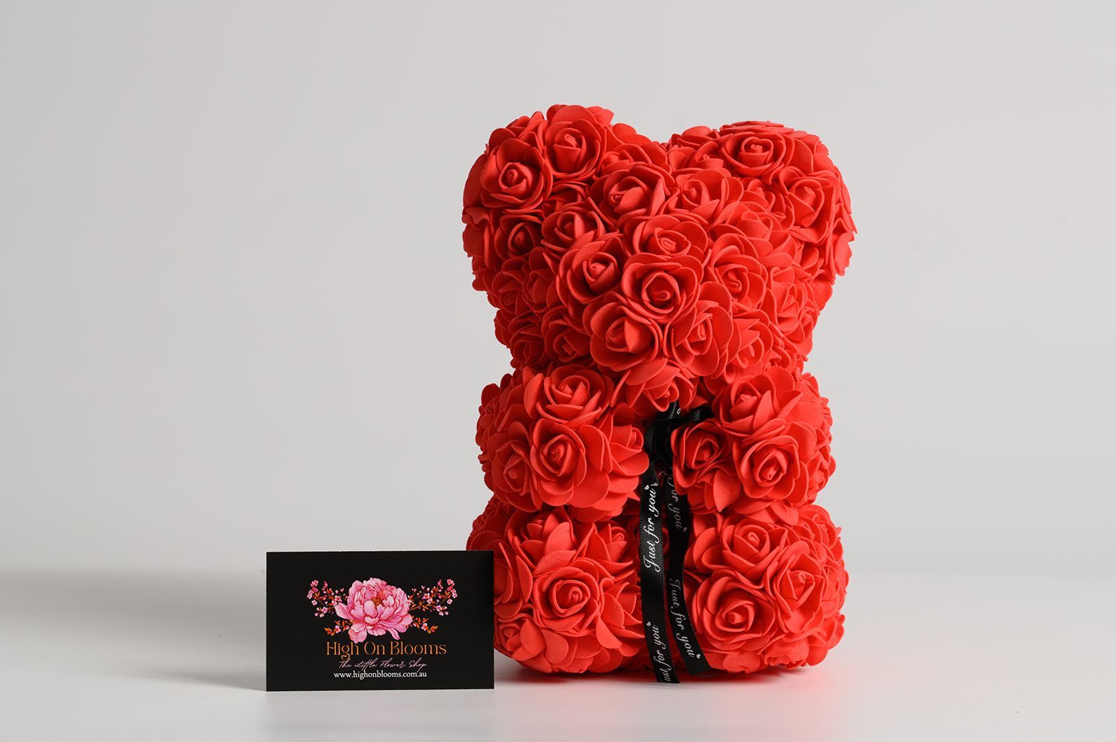 Red rose bear with a heart-shaped head, sitting next to a business card on a white surface.