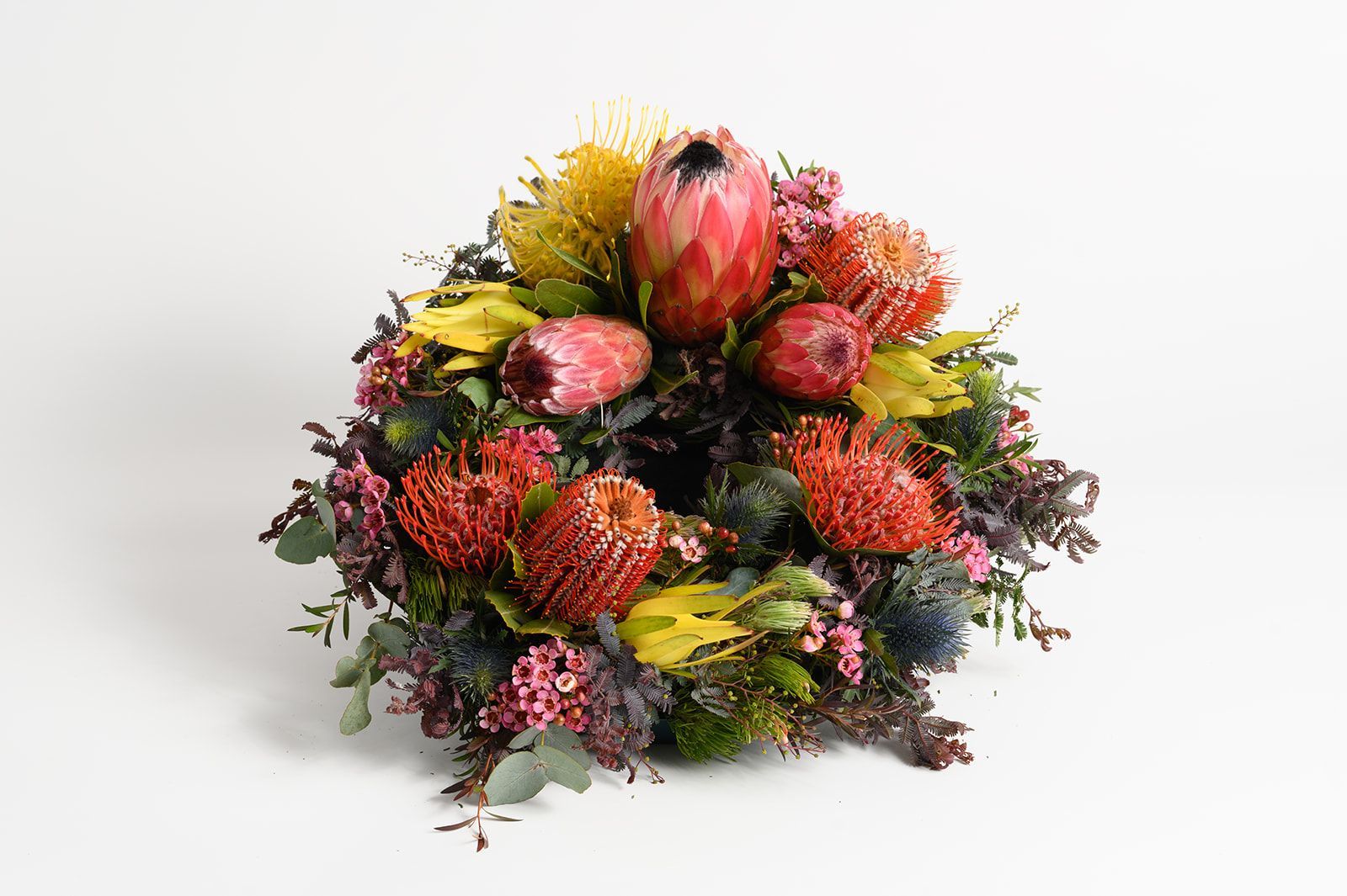 Colorful wreath of native flowers with pink, red, yellow, and orange blooms on a white background