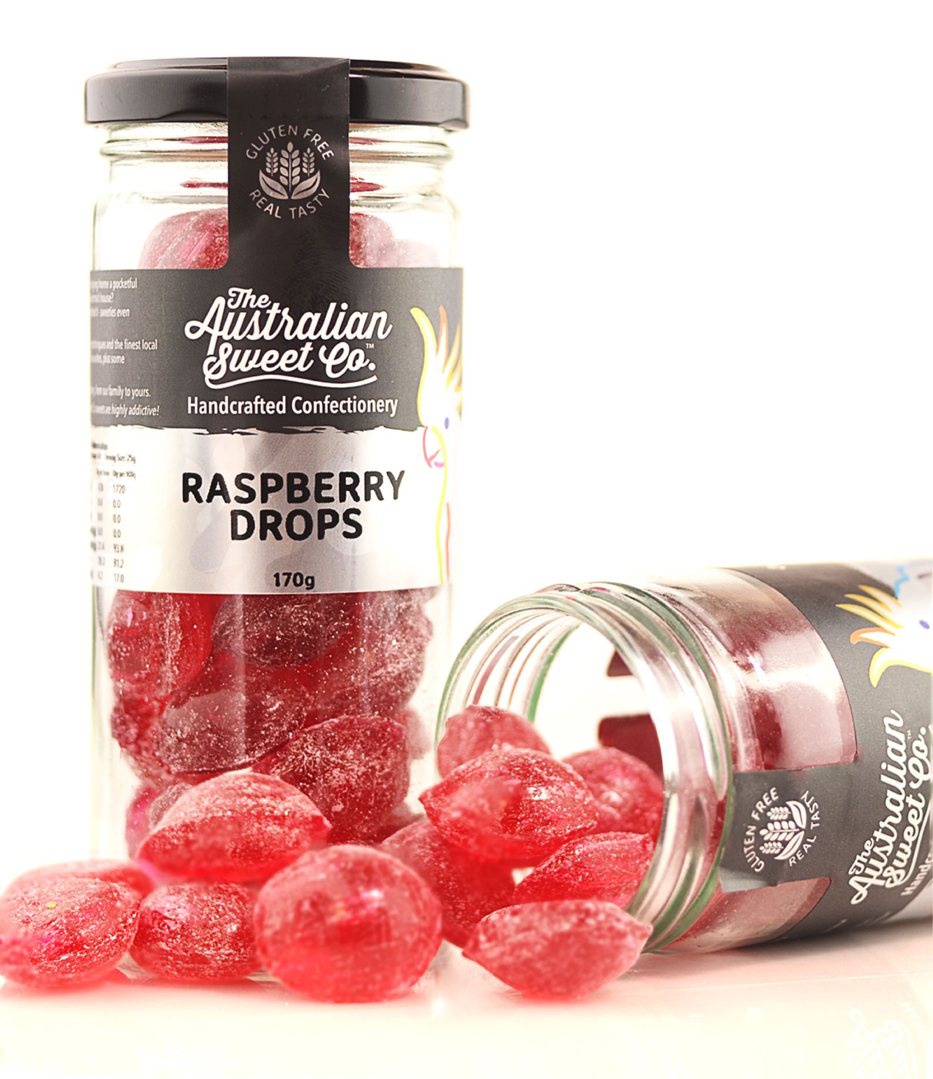Jar of raspberry drops candy with red sweets spilling out beside it