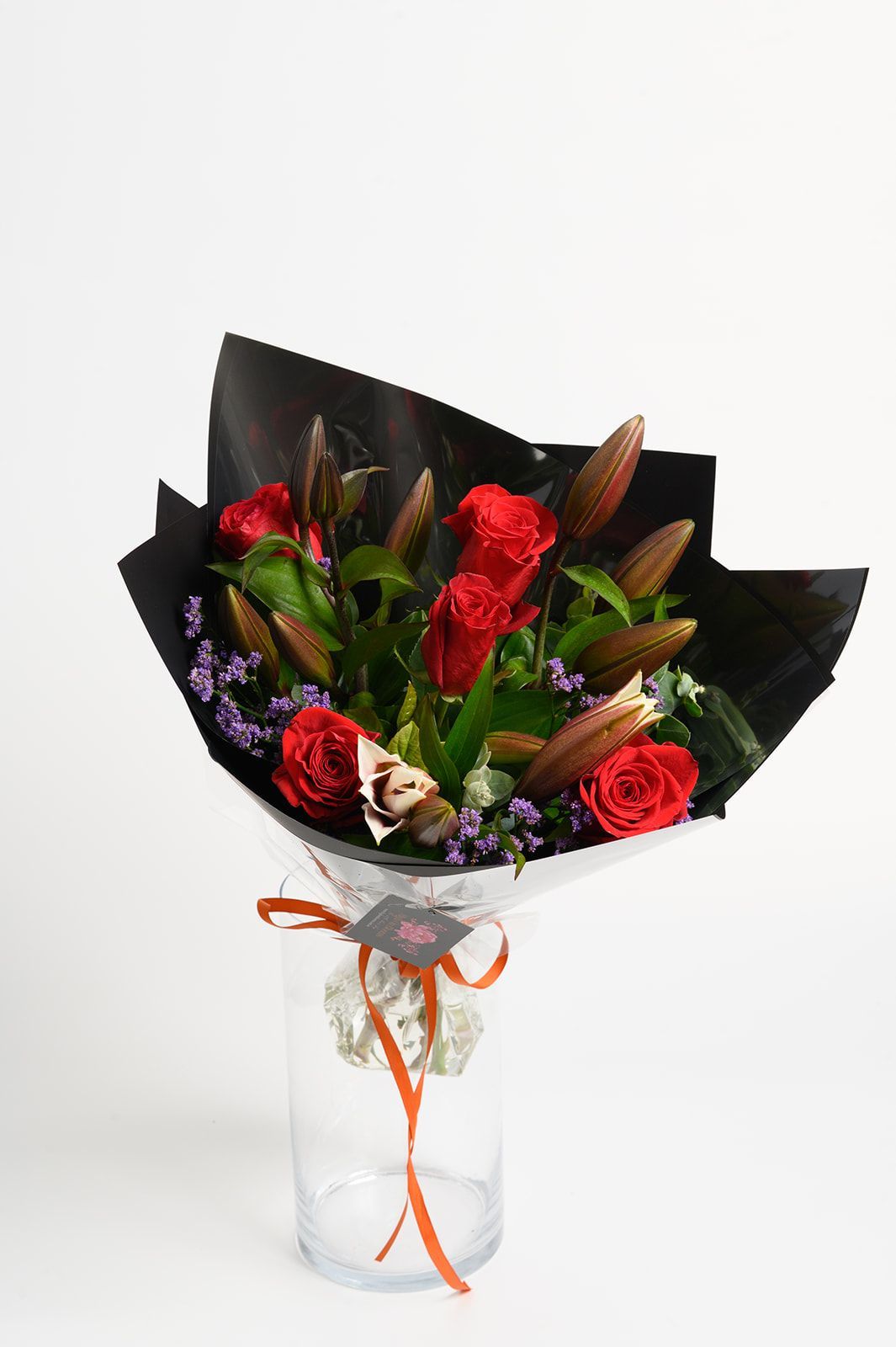 Bouquet of red and purple flowers wrapped in black paper with orange ribbon in a clear vase