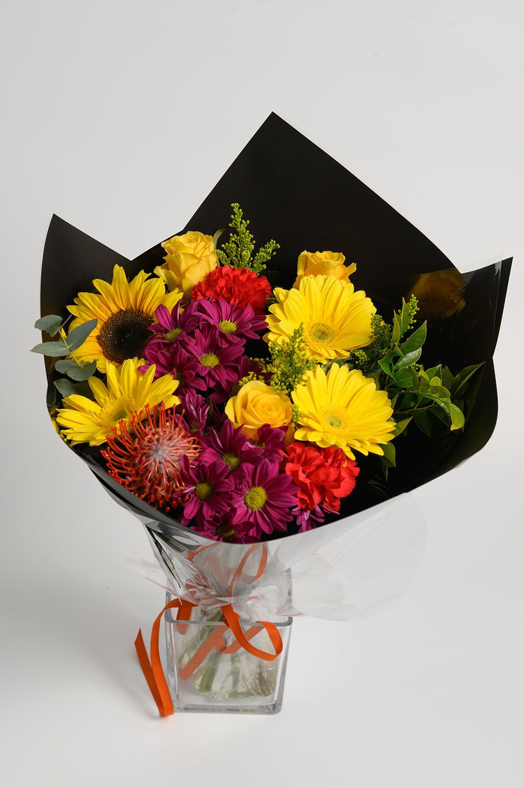 Bouquet of yellow, magenta, and orange flowers wrapped in black paper, tied with orange ribbon