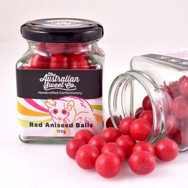 Jar of red aniseed balls with some spilled out on a white surface, Australian Sweet label visible