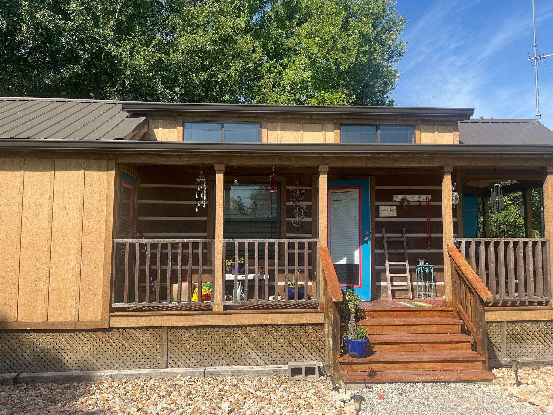 Tan tiny home with a brown porch and teal door, steps, and small blue flower pot.