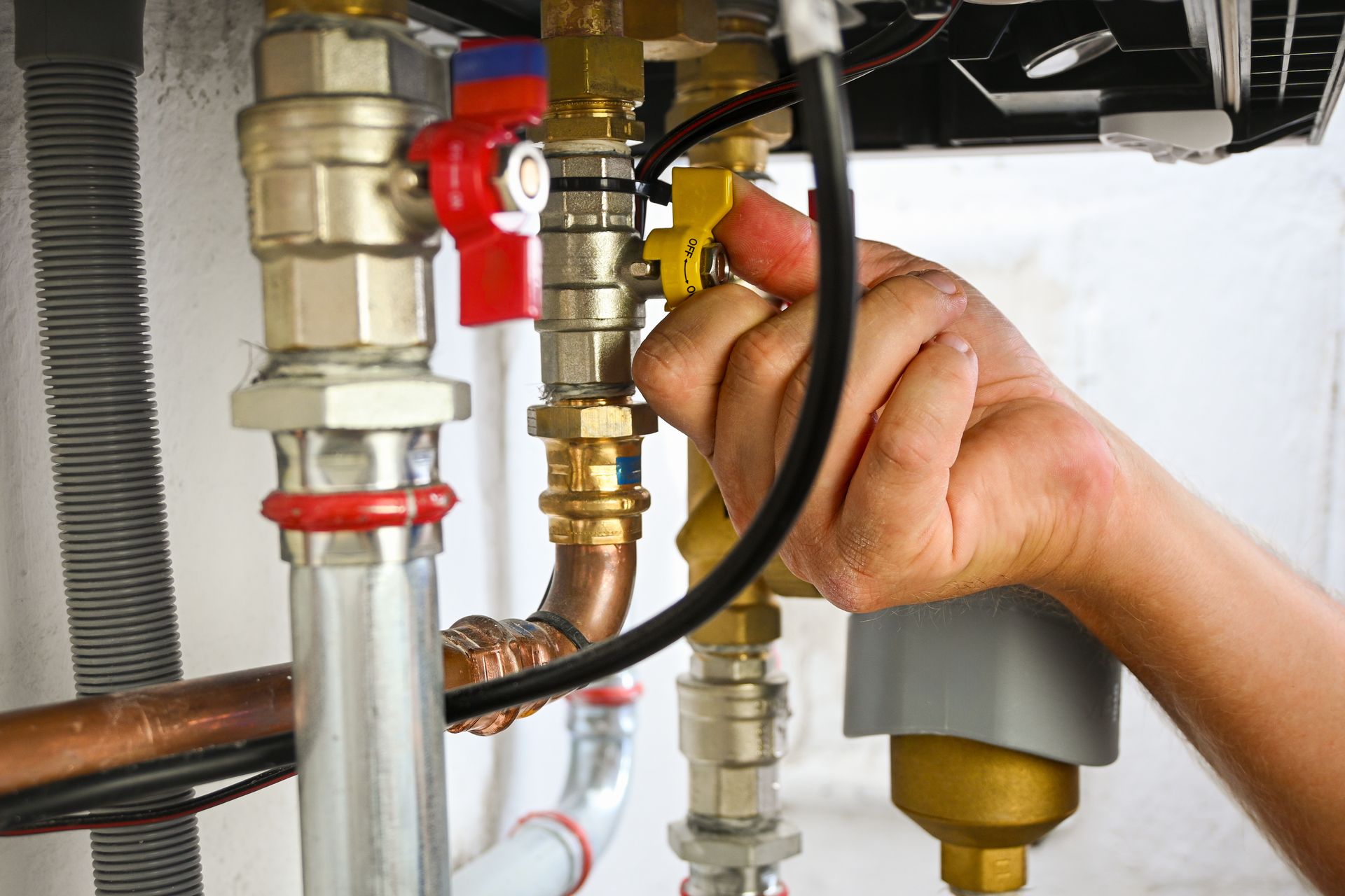 A hand turns a yellow valve handle on a complex plumbing assembly connected to a wall-mounted boiler. A hand turns a yellow valve handle on a complex plumbing assembly connected to a wall-mounted boiler.