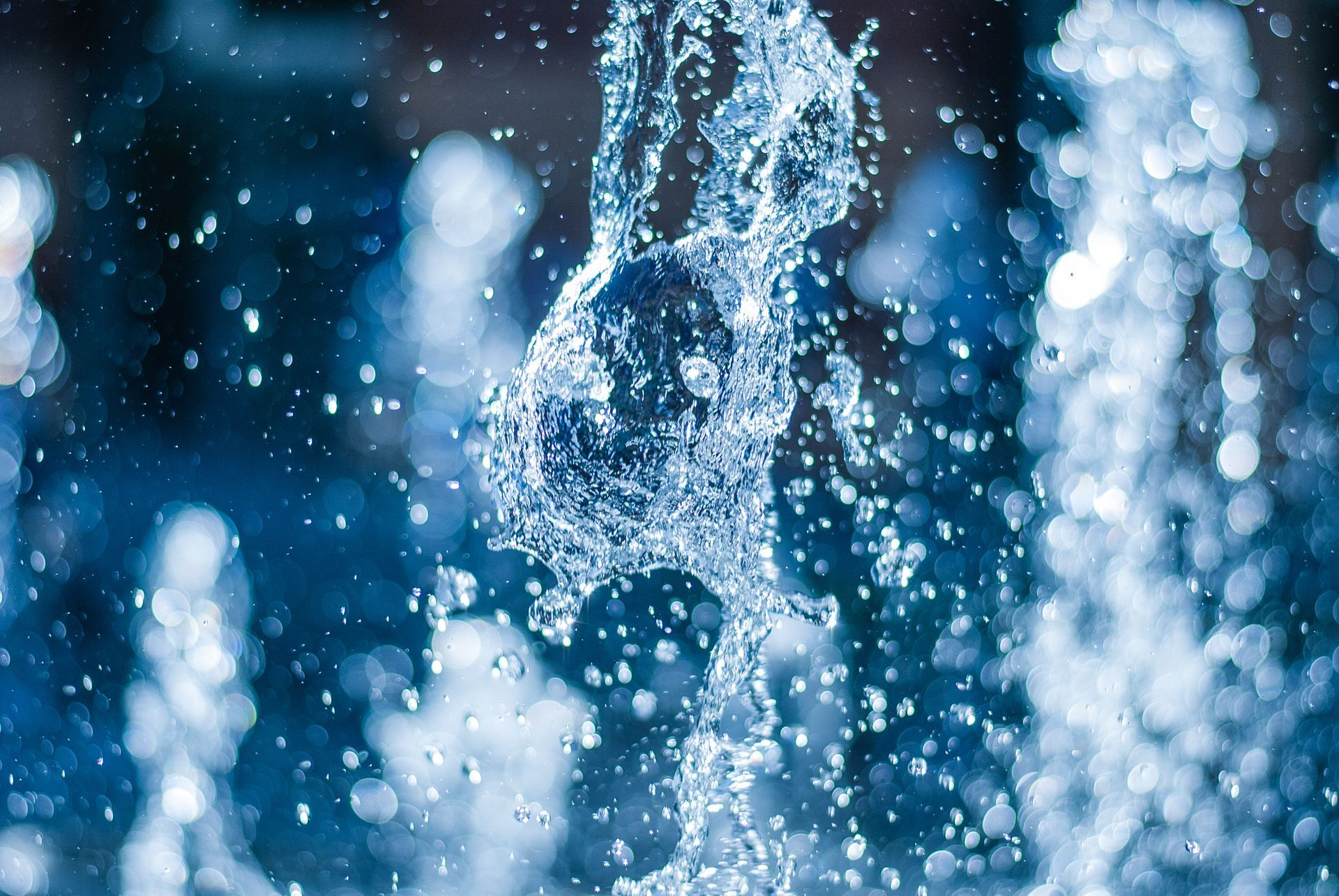 A close-up, high-speed capture of water splashing and droplets spraying against a blurred, deep-blue background. A close-up, high-speed capture of water splashing and droplets spraying against a blurred, deep-blue background.