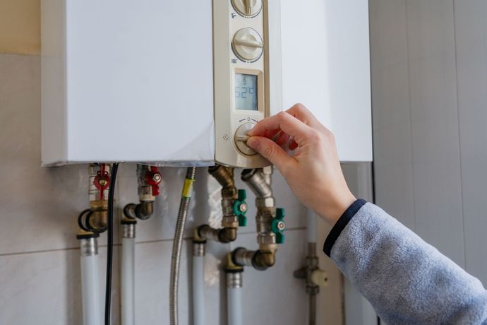 A technician in safety gear uses a wrench to adjust a wall-mounted heating system manifold with copper and white pipes. A technician in safety gear uses a wrench to adjust a wall-mounted heating system manifold with copper and white pipes.