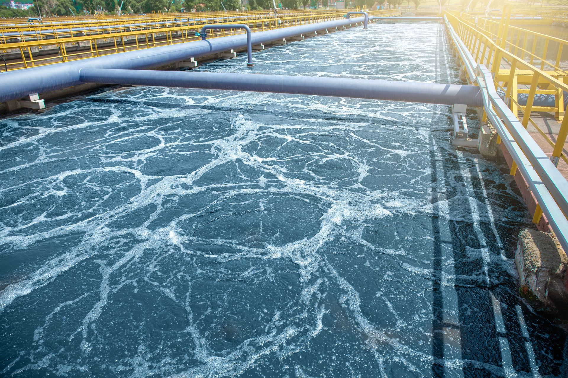 An aeration tank in a wastewater treatment plant with bubbly, agitated water and industrial pipes. An aeration tank in a wastewater treatment plant with bubbly, agitated water and industrial pipes.