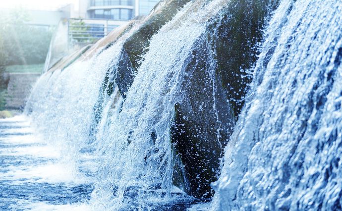 Water flows over a tiered concrete weir or spillway, creating cascading falls in a bright, outdoor setting. Water flows over a tiered concrete weir or spillway, creating cascading falls in a bright, outdoor setting.