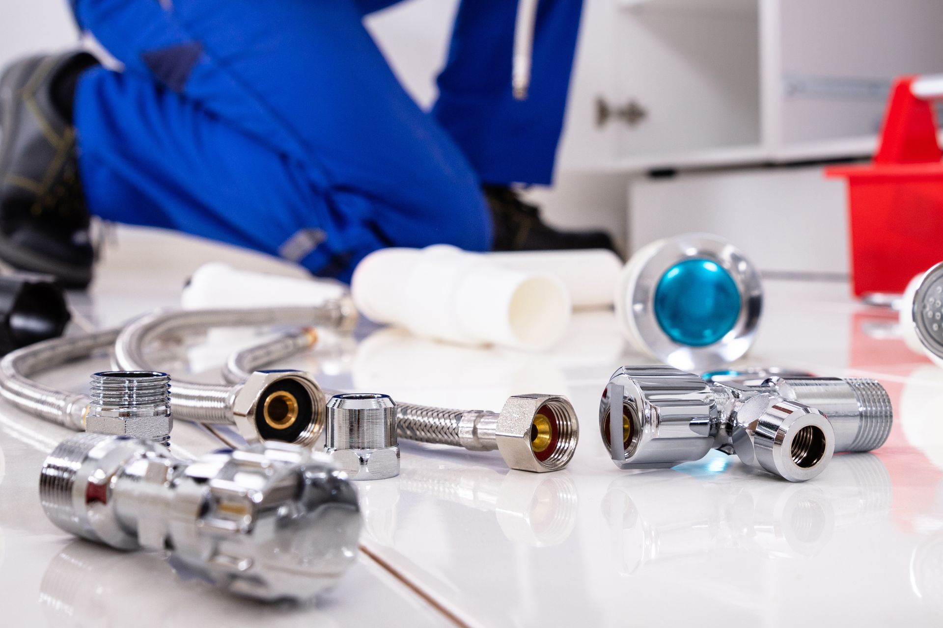 A technician in blue coveralls works near plumbing supplies, including metal pipes and valves, on a white tiled floor. A technician in blue coveralls works near plumbing supplies, including metal pipes and valves, on a white tiled floor.