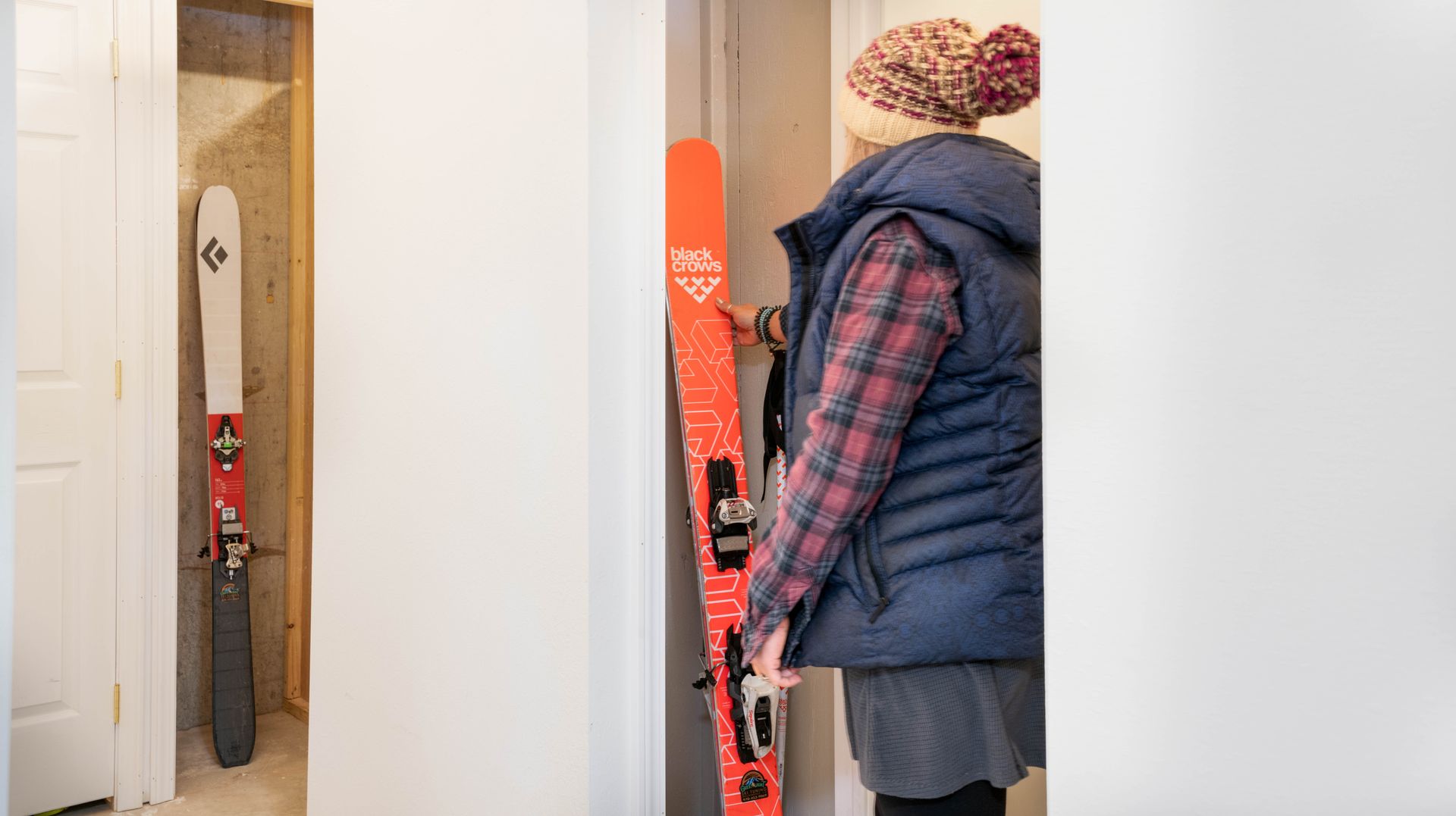 A woman is standing next to a pair of skis in a closet.