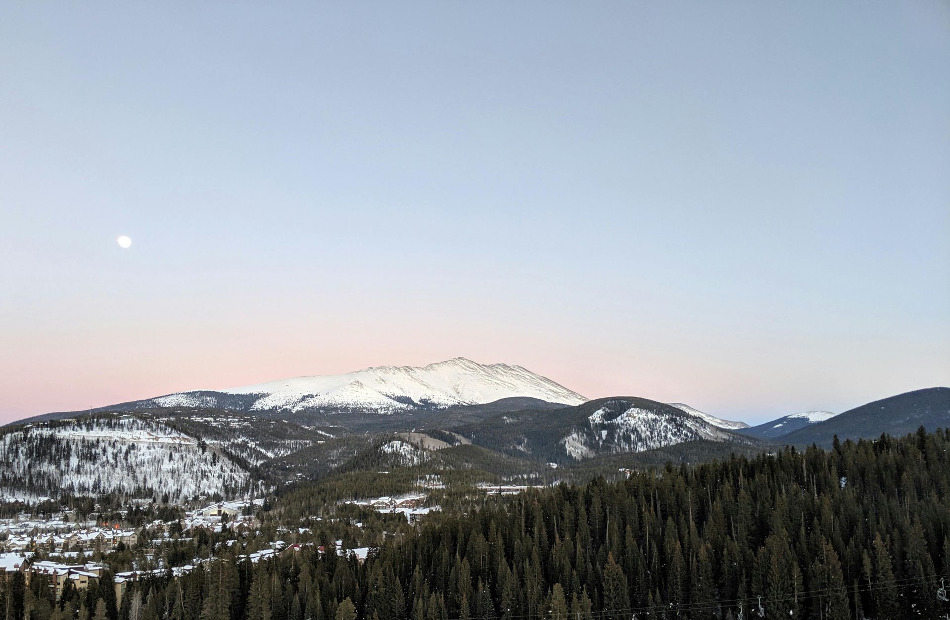 A mountain covered in snow is surrounded by trees and a full moon in the sky.