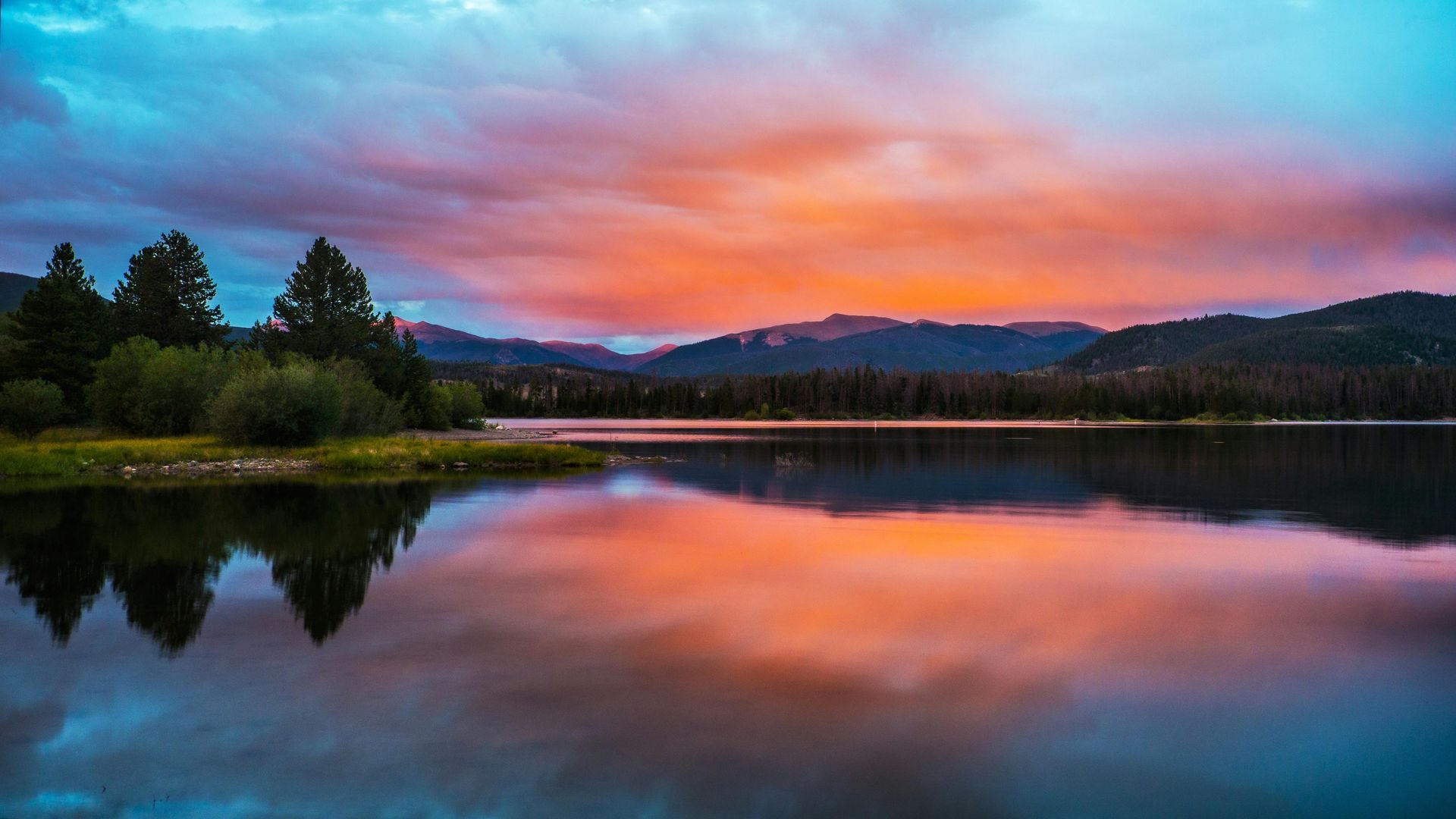 There is a sunset over a lake with mountains in the background.