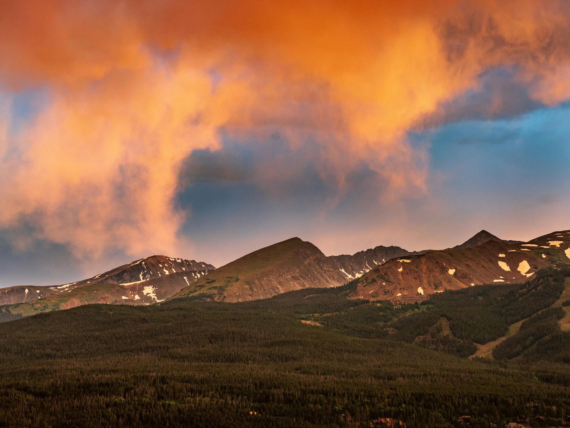 A mountain covered in trees with a cloudy sky in the background.