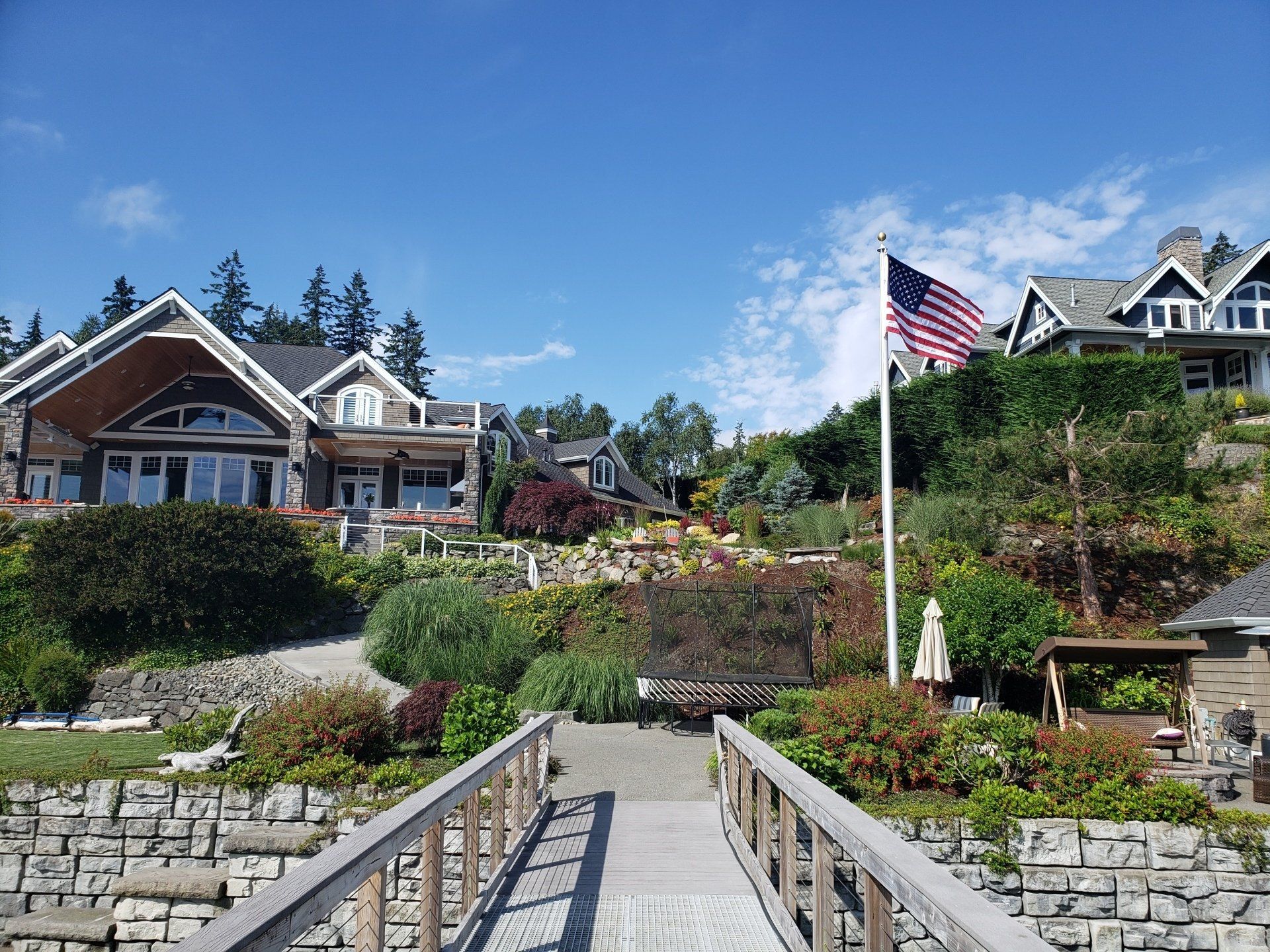 Wooden dock leading to waterfront homes with an American flag on a sunny day.