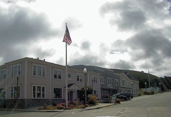 Buildings on a hillside with an American flag under a cloudy sky.