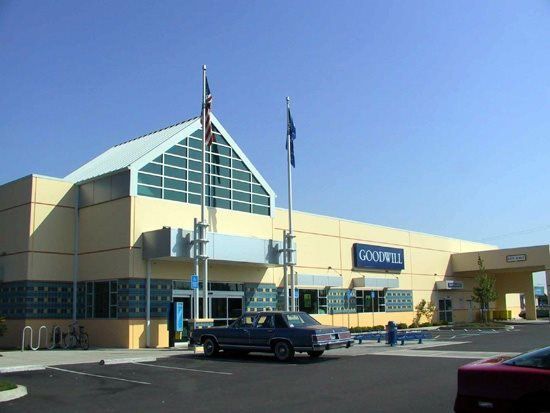 Goodwill store with blue and yellow exterior, blue car in parking lot, two flag poles.