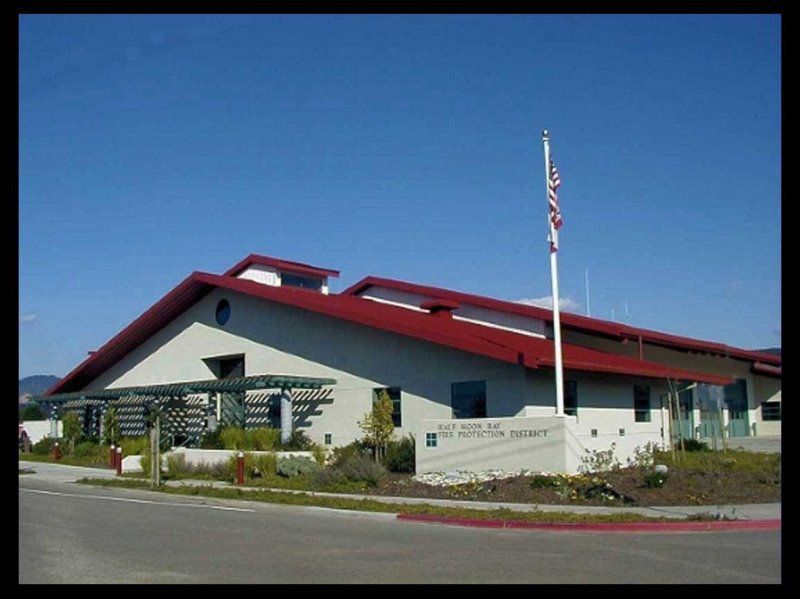 Exterior of the Soquel Library, a light-colored building with a red roof, American flag, and clear blue sky.