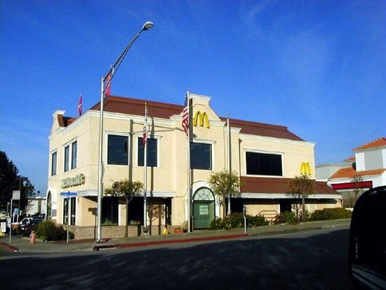 McDonald's restaurant in a beige building with a red tile roof, American flags, and the McDonald's logo.