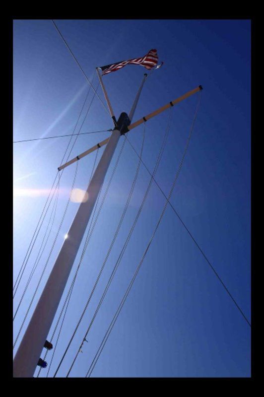 White sailboat mast with American flag against a clear blue sky.