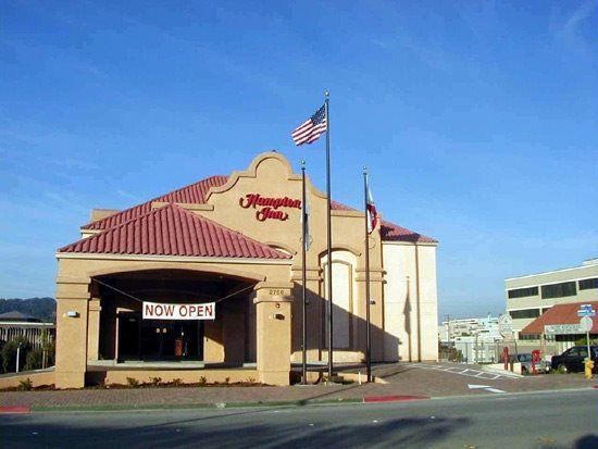 Hampton Inn hotel building with red tile roof and American flag against a clear blue sky.