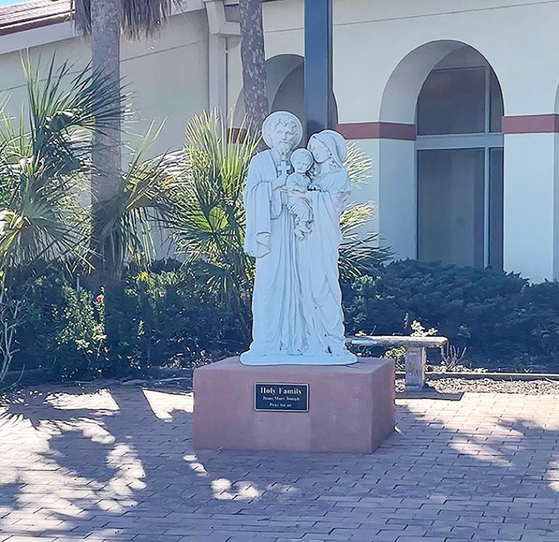White religious statue on a pedestal in a sunny courtyard with arches and palm plants