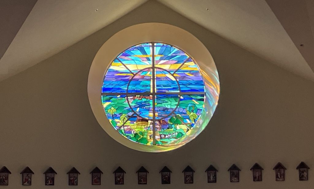 Circular stained-glass window with a colorful landscape design in a vaulted ceiling