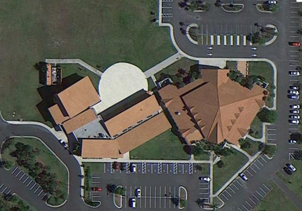 Aerial view of a tan-roofed building surrounded by parking lots and roads.