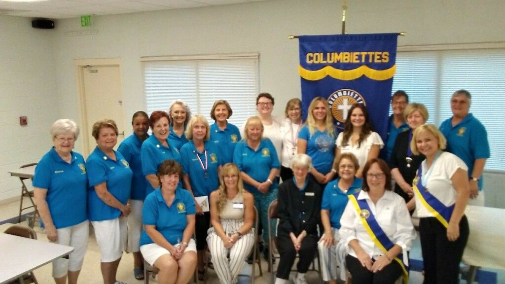 Group of people in blue shirts posing indoors with a “CLUBETTES” banner behind them.