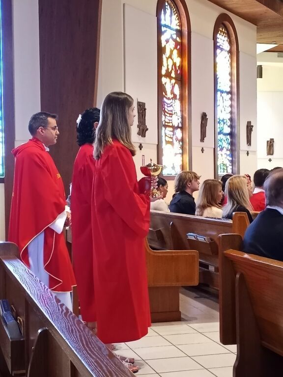 Two clergy in red robes standing in a church aisle beside seated congregants