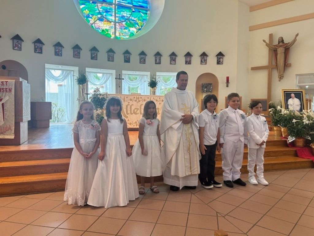 Children in white church attire pose with a priest inside a church sanctuary.
