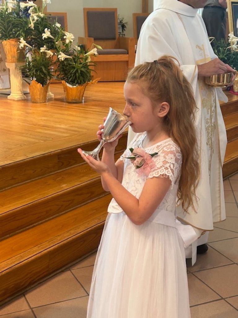 Young girl in a white dress holds a microphone at a church altar during a ceremony