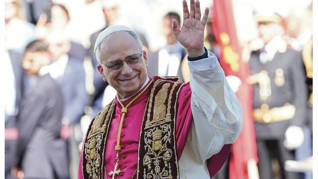 Smiling cleric in red and gold vestments waving to a crowd outdoors